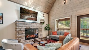 Una sala de estar acogedora con chimenea de piedra, sofá de cuero y un amplio ventanal con vistas a un área boscosa.