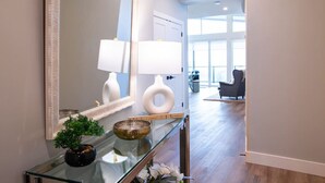 A modern interior with a glass console table, decorative items, and a large mirror. - The Luna | New Penthouse w Patio, Lake & Mtn Views (Harrison Hot Springs)