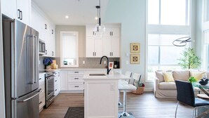 A modern kitchen with white cabinetry, stainless steel appliances, and a central island. - The Luna | New Penthouse w Patio, Lake & Mtn Views (Harrison Hot Springs)