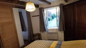Un dormitorio con cama, ventana con cortinas, armario de madera y lámpara colgante.