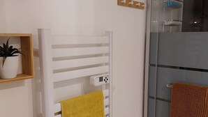 Un baño con un toallero blanco, una toalla amarilla, un box de ducha de cristal y una pequeña repisa con una planta.