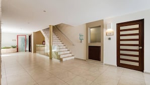 Un hall d’entrée spacieux avec un escalier, une porte portant un numéro et un détecteur d’incendie.