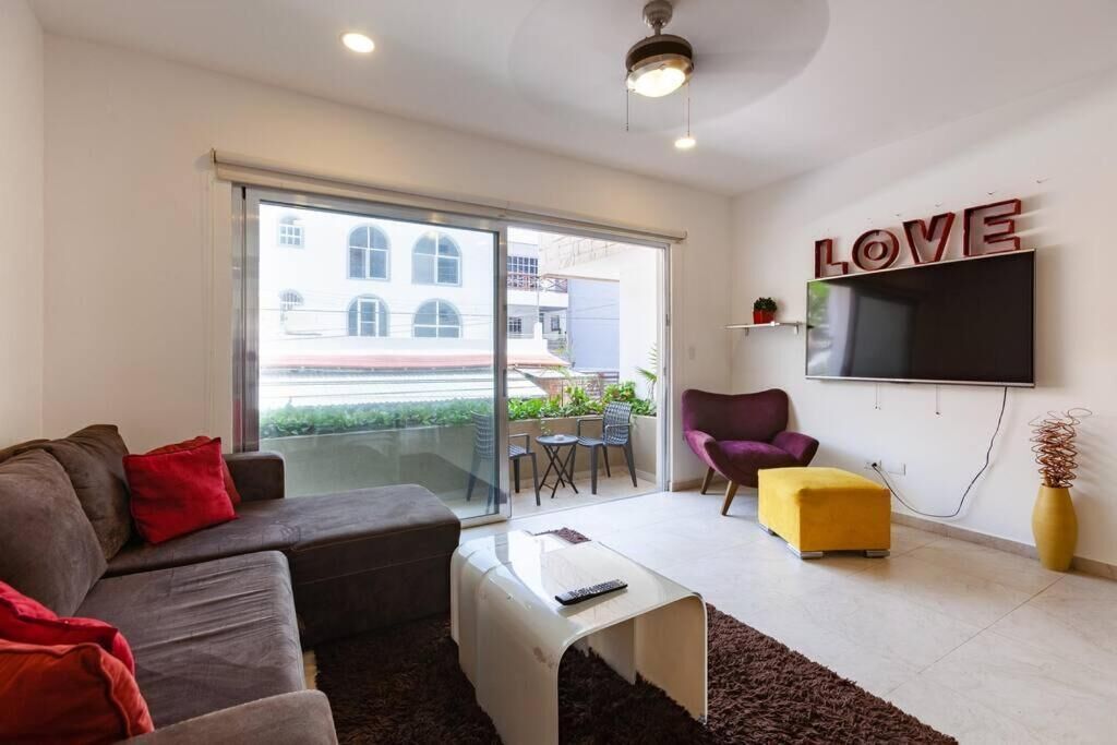 A modern living room with a sofa, a coffee table, a TV, and a sliding glass door leading to an outdoor area.