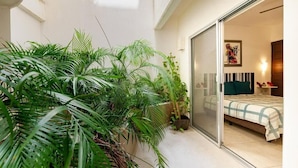 Une chambre à coucher moderne avec un lit, une porte-fenêtre coulissante et une grande plante en pot au premier plan.