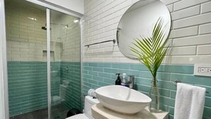 Une salle de bain comprenant des toilettes, un lavabo avec un receveur, un miroir et un espace douche doté de portes en verre.