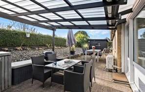 Une terrasse extérieure dotée d'un toit en verre, de meubles en osier et d'un barbecue.