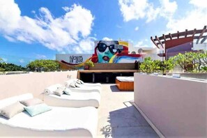 Un área de descanso en la azotea con sillones blancos y un mural colorido en la pared.