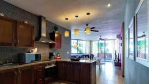 Eine moderne Küche mit dunklen Holzsäulen, einer Mikrowelle und einer Kaffeemaschine. Eine große Kücheninsel mit Spüle und Deckenventilator.