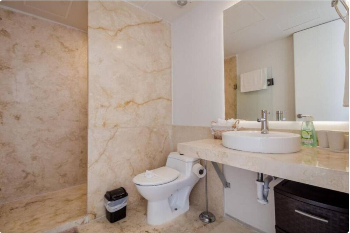 A bathroom with a marble floor, a white toilet, a sink with a mirror above it, and a trash bin.