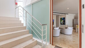 A staircase with a metal handrail leading to a room with a white wicker sofa and a painting on the wall. - Magia by Zamá Homes (Playa del Carmen)