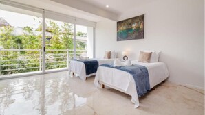 A bedroom with two beds, a large window, and a painting on the wall. - Magia by Zamá Homes (Playa del Carmen)