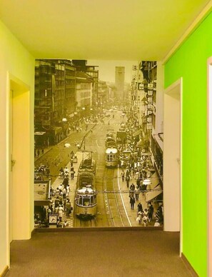 A corridor with a vintage street scene mural on the wall, featuring trams and pedestrians.
