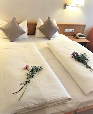 A hotel room with two beds, each with white linens and pillows, a bedside table with a phone, and a wall-mounted light. - Hotel Austria Stuttgart City (Stuttgart)