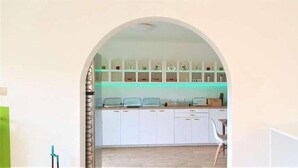 Una cucina con mobili bianchi, un piano di lavoro e una mensola sospesa con diversi oggetti.