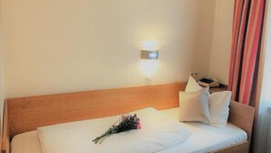 Camera d'albergo con testiera in legno, un comodino con telefono e lampada, e un bouquet di fiori sul letto.