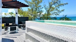 A poolside area with a pergola, outdoor seating, and a view of the ocean.