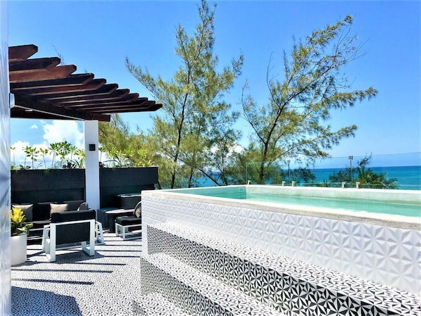 Un área junto a la piscina con una pérgola, mobiliario exterior y vista al océano.