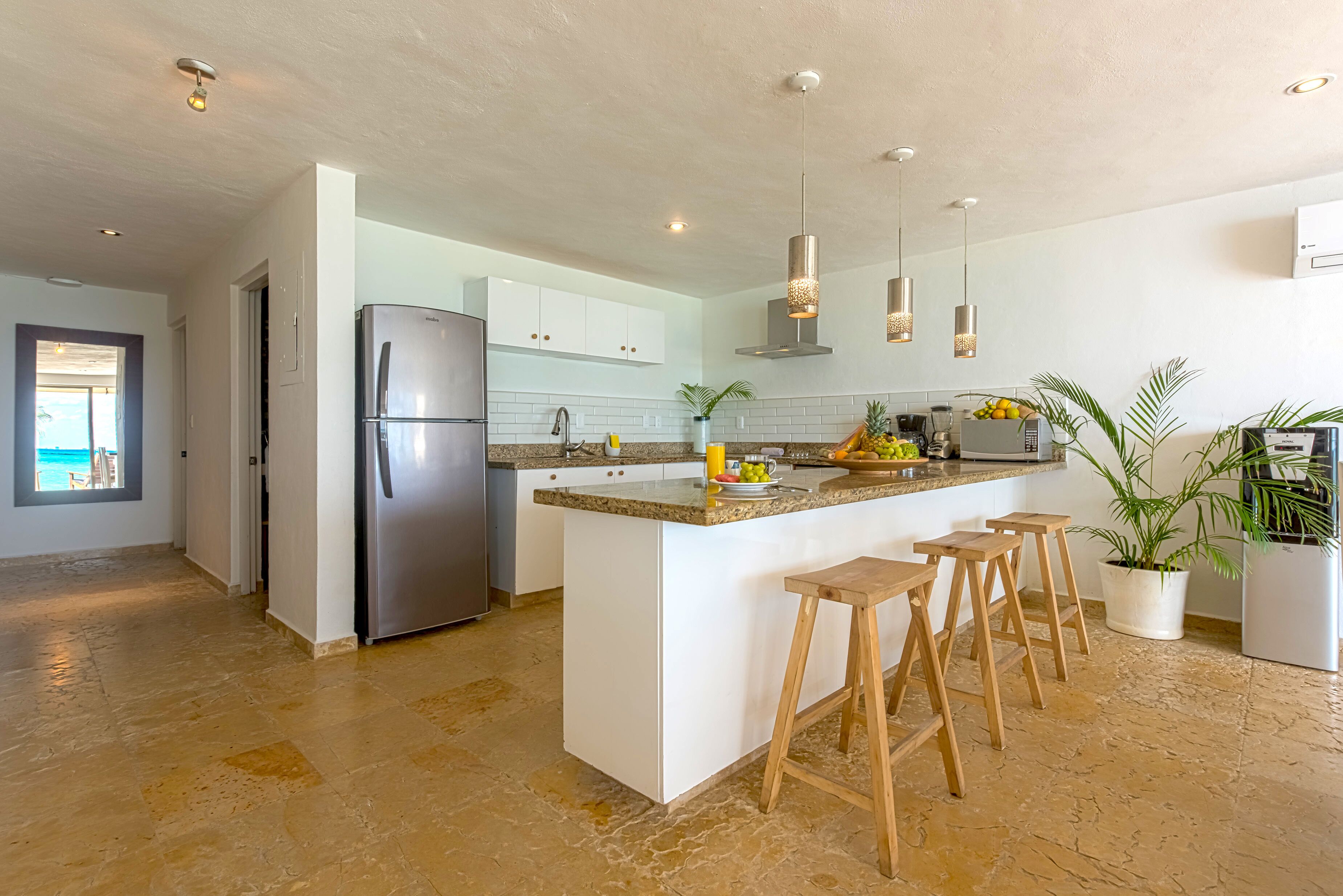 A modern kitchen with a central island, stainless steel appliances, and wooden bar stools.