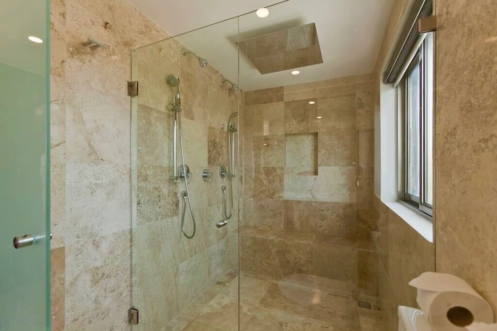A modern bathroom with a glass-enclosed shower, marble walls, and a window providing natural light.