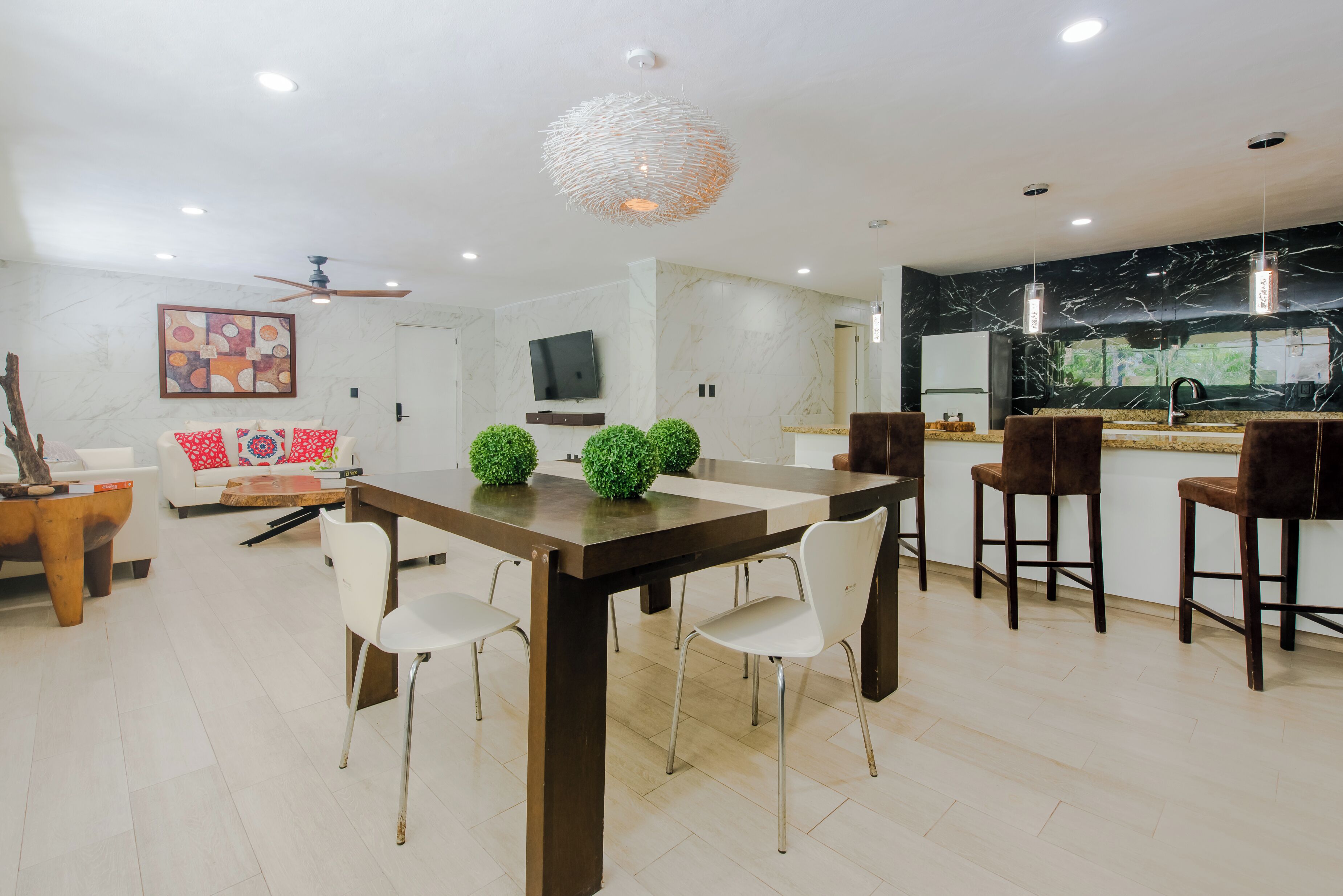 Uma cozinha moderna com painel de fundo de mármore, uma área de refeições com mesa e cadeiras de madeira, e um balcão com banquetas.