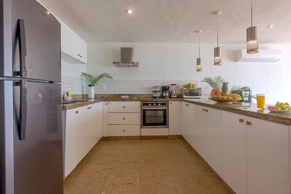 A modern kitchen with white cabinets, a stainless steel refrigerator, an oven, and a granite countertop.
