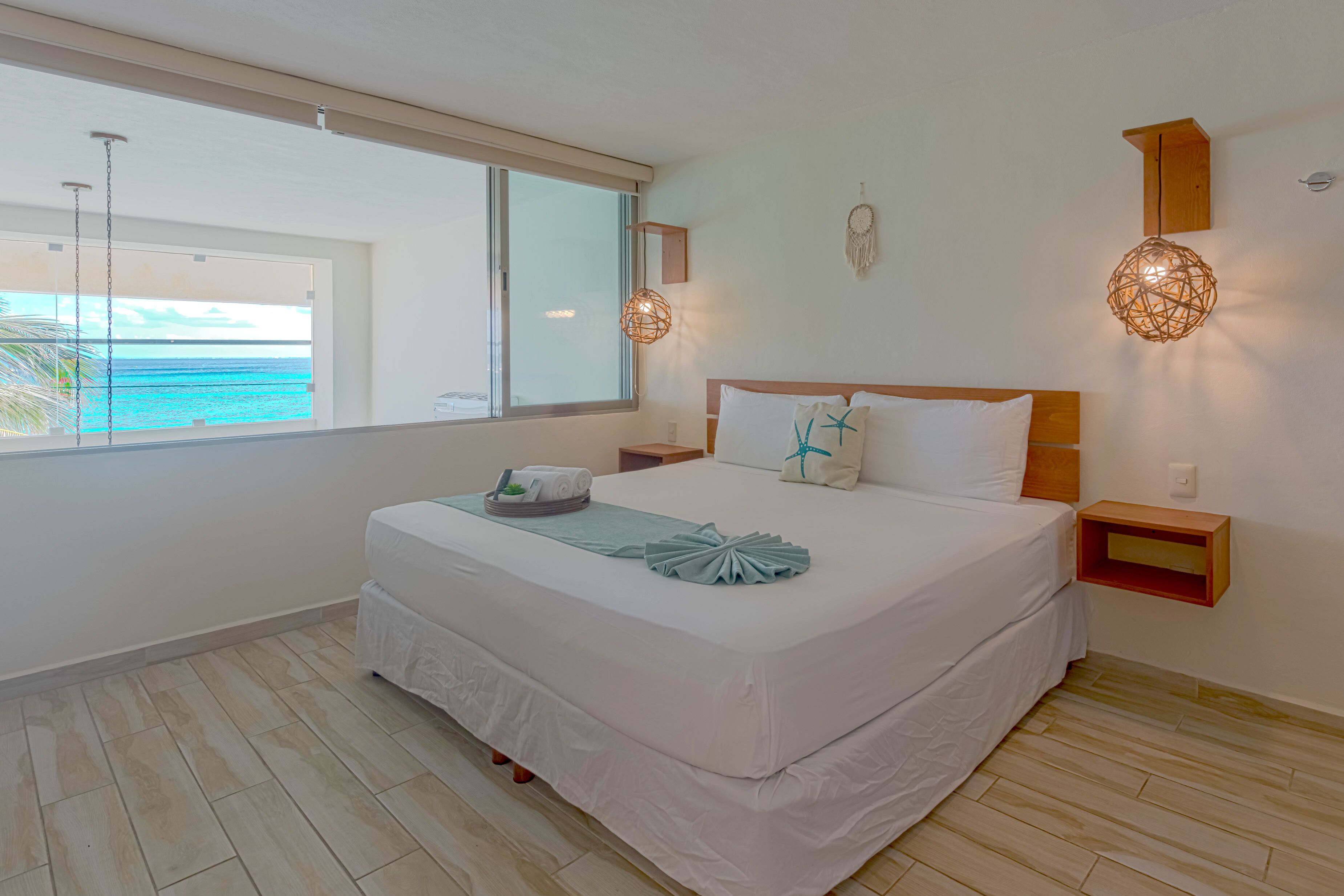 Ein Schlafzimmer mit großem Fenster, einem Bett mit weißer Bettwäsche, einem Nachttisch und einem an der Wand befestigten Regal.