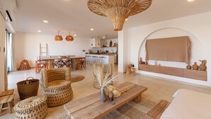A spacious living area with a dining table, wicker chairs, a large woven light fixture, and a cozy seating area with a bench and cushions.