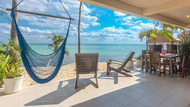 A hammock, chairs, and a table on a patio with a view of the ocean.