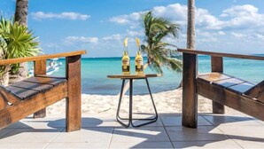 A wooden bench with a small table in the middle, placed on a tiled surface with a view of the beach and ocean.