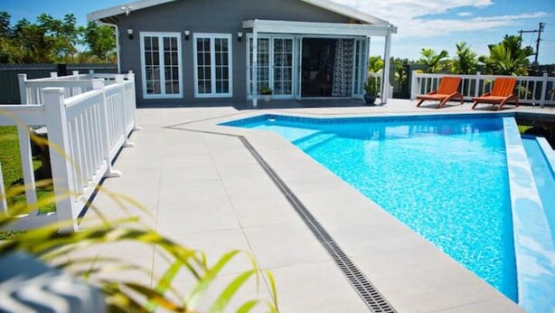 Ein modernes Haus mit Swimmingpool, einer überdachten Terrasse und einem eingezäunten Bereich mit Liegestühlen.