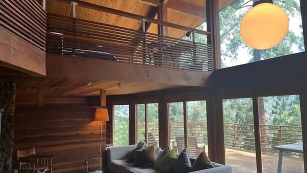A log cabin interior with a loft bedroom, large windows, and a hanging light fixture. - 4 Acre A-Frame Private Retreat (Idyllwild)