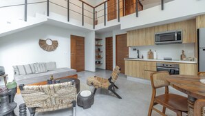 Amplia sala de estar con techo alto, cocina equipada con electrodomésticos modernos y una mesa de comedor.