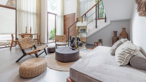 Una sala de estar amplia con un sofá, una mesa redonda de centro y un comedor con sillas y una mesa. Una escalera conduce a un nivel superior.