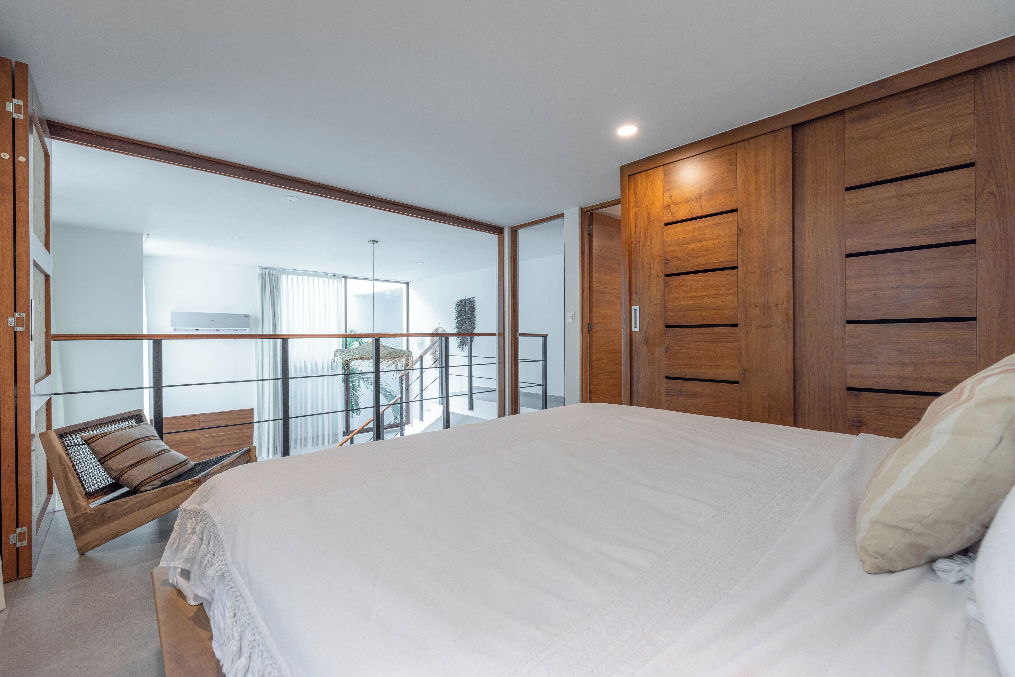 Quarto com cama grande, armário de madeira e varanda com vista para o exterior.