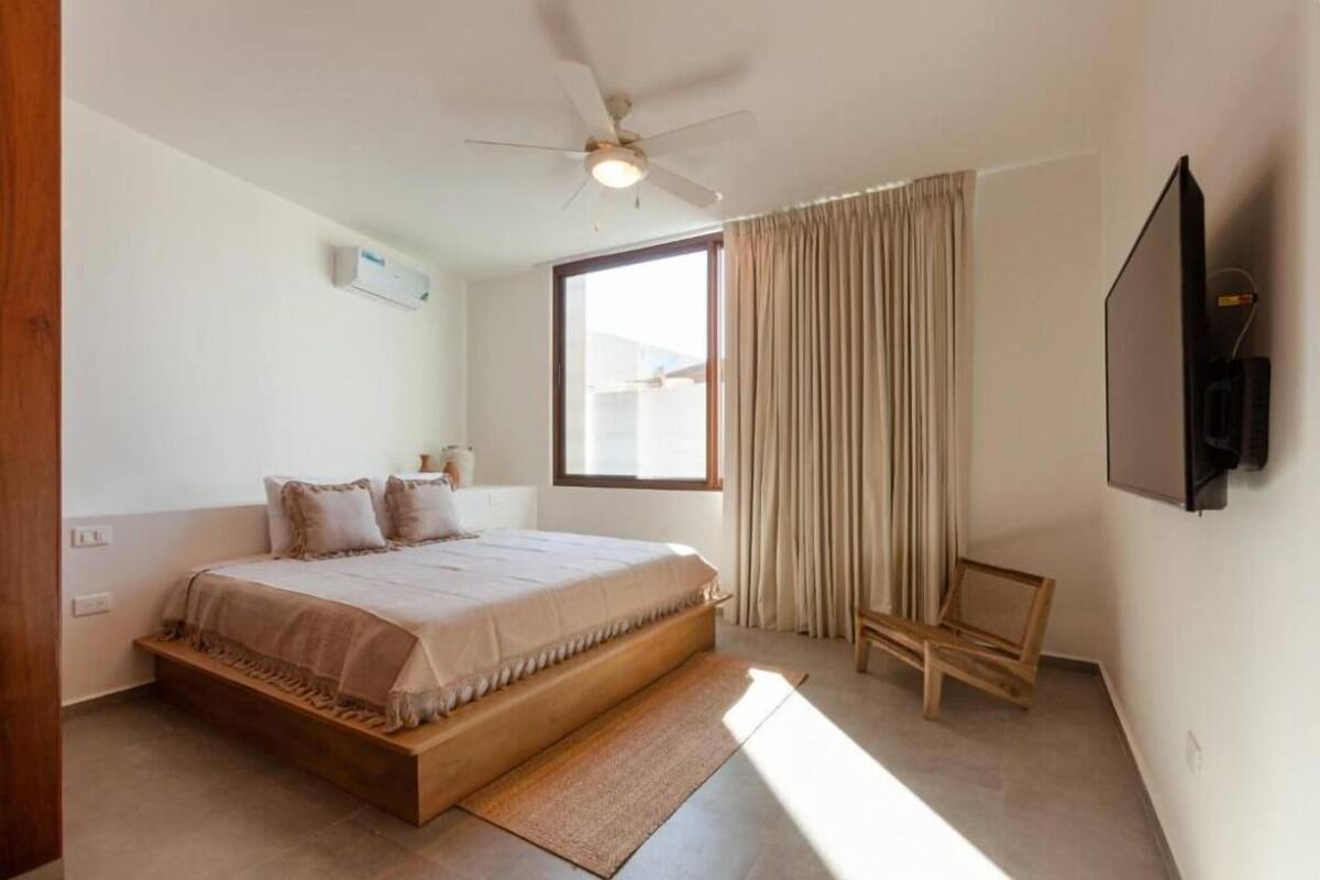 Un dormitorio con cama, ventilador de techo, televisión y ventana con cortinas.