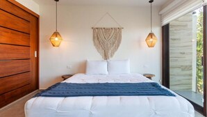 Un dormitorio moderno con una cama grande, dos lámparas colgantes y un tapiz de macramé en la pared.