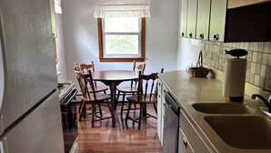 A kitchen with wooden cabinets, a refrigerator, a dining table with chairs, a window, and a sink. - Cozy 2-bedroom cabin between Levering and Cheboygan on Lancaster Lake (Levering)