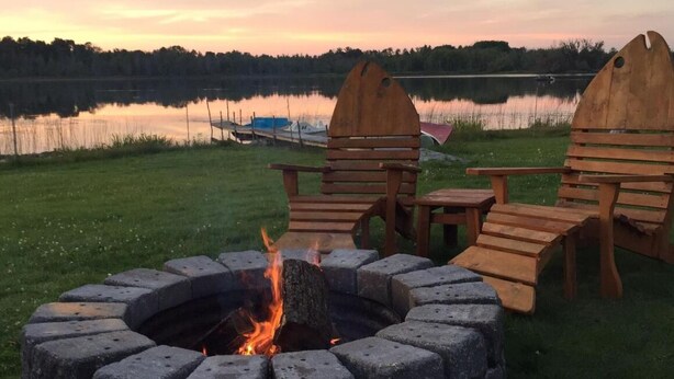 A fire pit with stone seating and a view of a lake at sunset. - Cozy 2-bedroom cabin between Levering and Cheboygan on Lancaster Lake (Levering)