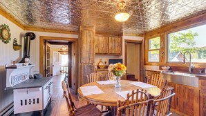 A rustic kitchen with wooden cabinets, a farmhouse stove, and a dining area with a round table and chairs. - Pellston Farmhouse w/ Snowmobile Trail Access! (Pellston)