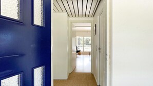 A hallway with a blue door, white walls, and a view to a balcony with a chair.
