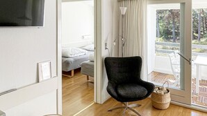 A modern room with a bed, a black chair, a TV, and a balcony with a view of trees.