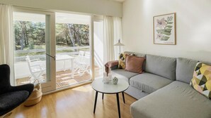 A living room with a sofa, a small round table, a chair, and a view through a sliding glass door to an outdoor area with a table and chairs.