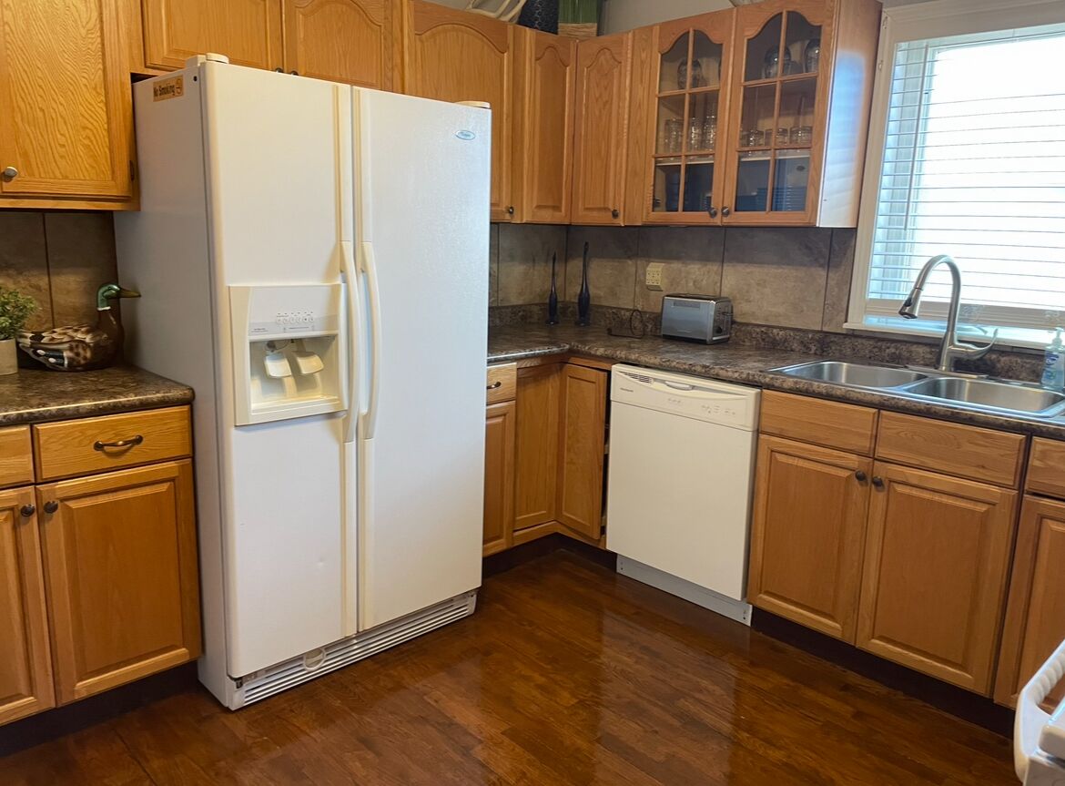 A kitchen with wooden cabinets, a white refrigerator, a dishwasher, and a granite countertop.