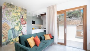 Een moderne woonkamer met een groene bank, een keukenhoek en een groot raam met gordijnen.