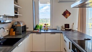 Eine moderne Küche mit weißen Schränken, einem eingebauten Ofen, einer Mikrowelle und einem Fenster mit Blick auf die Stadt.