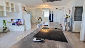 Ein modernes Wohnzimmer mit großem Flachbildfernseher, integriertem Herd und Essbereich mit langem Tisch.