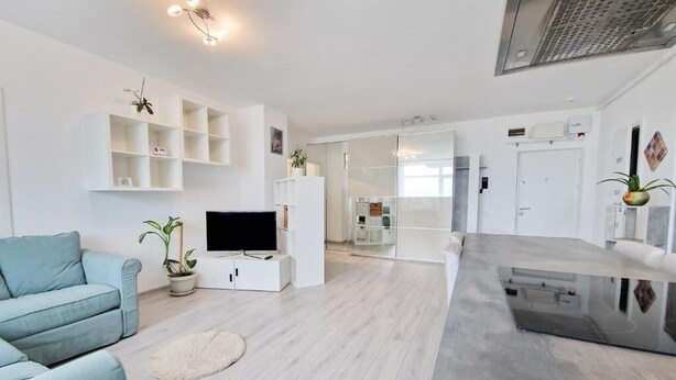 Ein modernes Wohnzimmer mit Flachbildfernseher, hellblauem Sofa und weißen Regalen.