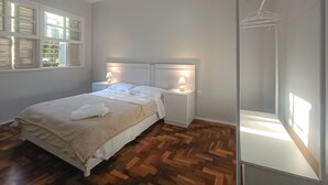 A bedroom with a bed, bedside tables, a ceiling fan, and a window with shutters. - Cozy apartment, great location with garage (Centro Histórico Porto Alegre)