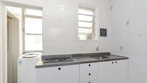 A modern kitchen with white cabinets, a granite countertop, a built-in oven, and a window with blinds. - Cozy apartment, great location with garage (Centro Histórico Porto Alegre)