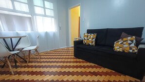 A living room with a black sofa, patterned cushions, a white table, and a chair. - Cozy apartment, great location with garage (Centro Histórico Porto Alegre)